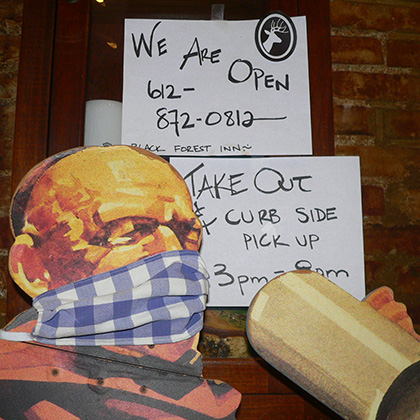 The Monk, wearing a custom BFI mask, with signs stating that we're open.